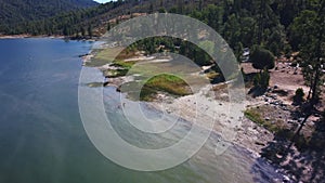 Falling drone footage of dark blue Bass lake and surrounding forests in California
