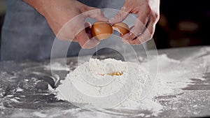 Falling egg into flour. Close up view of man hands breaking cracking raw egg over flour, baking concept. Baker kneads