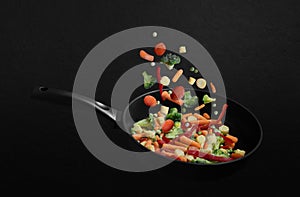 Falling frozen vegetables in a frying pan on black background. Vegetable mix flying down. Healthy natural food