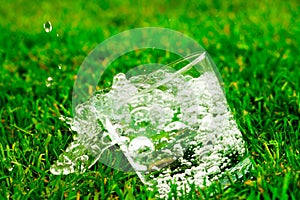 A falling glass of water or lemonade on grass background. Water with splashes and drops flows from a glass.