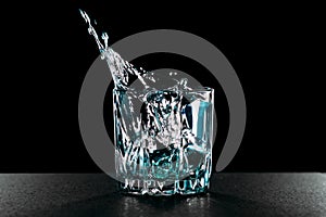 Falling ice cubes into a glass with gin. Glass with alcohol on a black background. Splashes of liquid