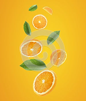 Falling juicy oranges with green leaves on orange background. Flying defocusing slices of oranges. Applicable for fruit juice