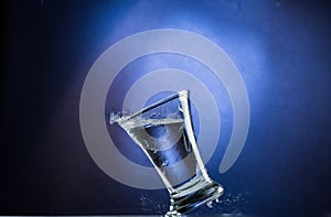 Falling and jumping glass with spilling liquid on a blue gradient background