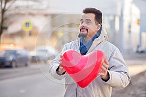 Falling in love metaphor: portrait of a smiling bearded adult man holding with two hands and giving away big red heart shaped air