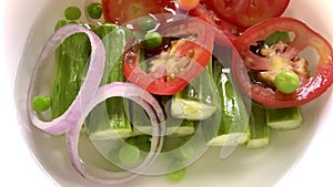 Falling of onion rings tomato slices organic peas and carrots into water