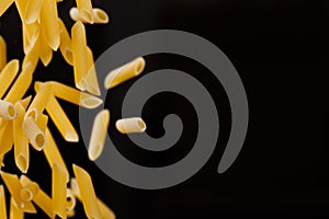 Falling penne pasta. Flying yellow raw macaroni over black background.