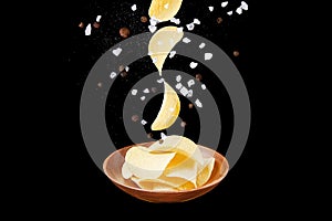 Falling potato chips into wooden plate filled with chips isolated on black background