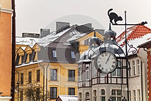 falling snow on the background of old houses, street clock and weather vane with the figure of a cat