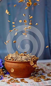 Falling sugar cornflakes in a ceramic bowl close-up top view. light breakfast scattered on the table with blue flowers close-up