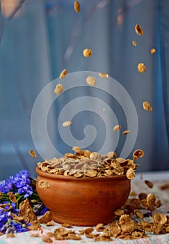 Falling sugar cornflakes in a ceramic bowl close-up top view. light breakfast scattered on the table with blue flowers close-up