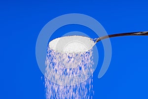 Falling sugar from a spoon on a blue background