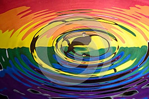 A falling water drop reflected in the circular waves from a splash and the colours and logo of Extinction Rebellion Gay Pride flag