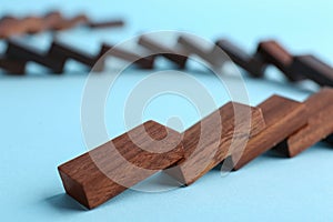 Falling wooden domino tiles on light blue background, closeup
