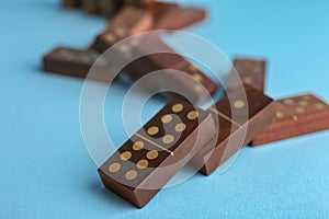 Falling wooden domino tiles on light blue background, closeup