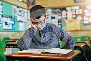 He always falls asleep when reading that book in class. an elementary school boy sleeping at his desk in class.