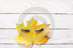 False eyelashes and autumn leaf on a light wood background
