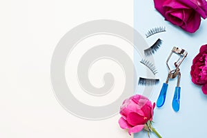 False Eyelashes and eyelash curler on blue background with pink flowers and white background with a copy space