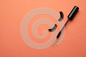 False eyelashes and mascara on orange background. Space for text