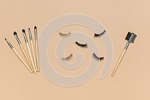 False eyelashes and a set of brushes on a beige background