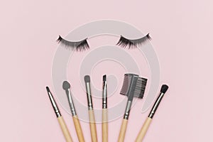 False eyelashes and a set of makeup brushes on a pink background