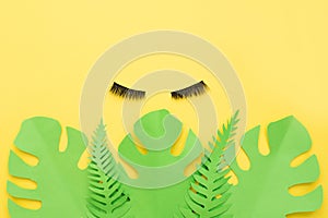 False eyelashes on summer yellow background with paper palm leaves with a copy space