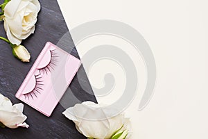 False eyelashes and white roses on background with copy space. Female accessories