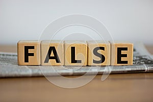 False in news symbol. Cubes placed on a newspaper form the word `false`. Beautiful wooden table. White background. Business and