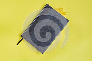 False reptile leather notebook of black color with maple leaf as bookmark on yellow background. Minimal flat lay