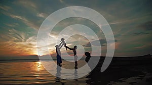 Famil play on a lake at sunset. Silhouettes of a little children and parents time together next, run and play. Slow