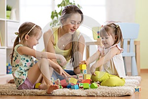 Family activities in the children room. Mother and her kids sitting on the foor playing