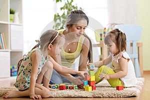 Family activities in the children room. Mother and her kids sitting on the foor playing