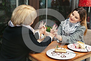 Family, an adult mother and daughter are sitting at a wooden table in a cafe on the street, looking at each other