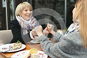 Family, an adult mother and daughter are sitting at a wooden table in a cafe on the street, looking at each other