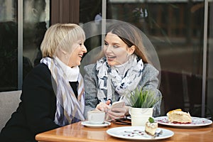 Family, an adult mother and daughter are sitting at a wooden table in a cafe on the street, looking at each other