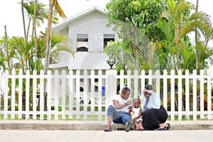 Family of African American people with young little daughter sitting in front of new house with white fence