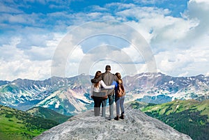 Family with arms around each other enjoying beautiful mountain view on hiking trip.