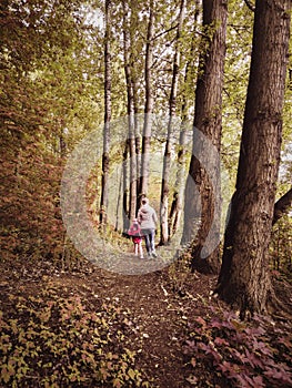 Family in autumn summer forest, back view. Woman and little girl walk away on path in woods. Child with mother go on footpath