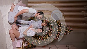 family with a baby boy in pajamas is sitting at the Christmas tree in the new year at home. Vertical. people are looking