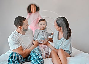 Family, baby and girl jump on bed in bedroom, having fun or playing. Support, love and care of happy father, mother and