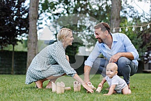Family with a baby playing in grass at family garden party. Father, mother, and a small child at birthday party.