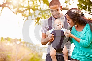 Family With Baby Son In Carrier Walking Through Park