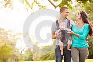 Family With Baby Son In Carrier Walking Through Park