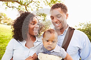 Family With Baby Son In Carrier Walking Through Park