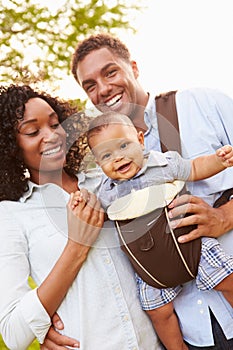 Family With Baby Son In Carrier Walking Through Park