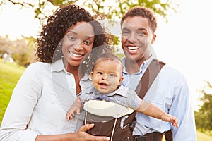 Family With Baby Son In Carrier Walking Through Park