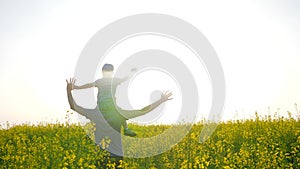 Family in backlight raising hands up plays in grass, son sits on shoulders father on meadow in sunny day, happy dad with