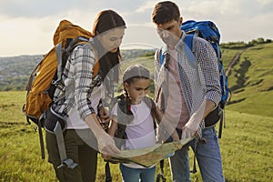 Family with backpacks look at the map are guided on a hiking trip in nature.