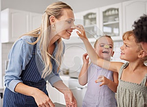 Family baking and mother teaching children to bake cake in the kitchen of their home. Happy girl kids and woman play