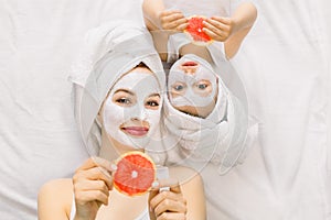 Family beauty treatment in the bathroom. Pretty mother and daughter baby girl make a clay mask for face skin, lying on