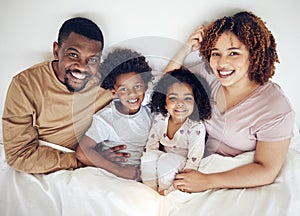Family, bed and happy portrait of a mother, father and children in a bedroom in the morning. Home, happiness and smile
